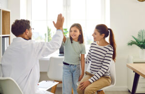 Friendly male pediatrician doctor giving high five to a little child girl patient standing at the doctor's office with her