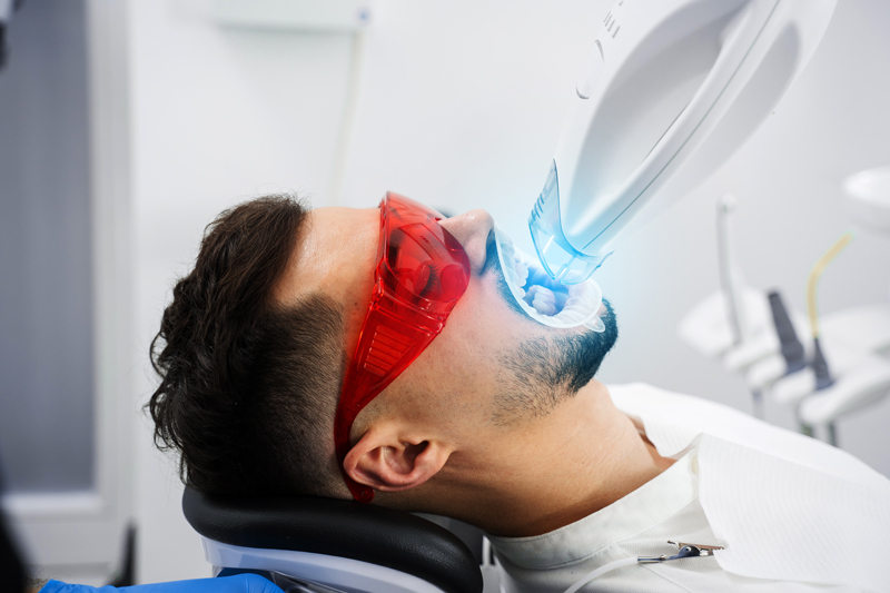 Patient whitens his teeth while treatment in dental cabinet. Ultraviolet teeth whitening procedure in dental clinic