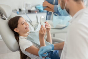 girl looking in the mirror after dental procedure while mother standing near her for support